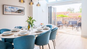 A dining area with a table set for six, blue chairs, and hanging pendant lights. - Seawood House, Wells-next-the-Sea, Norfolk (Wells-next-the-Sea)