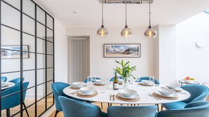 A dining area with a round table set for six, blue chairs, and hanging pendant lights. - Seawood House, Wells-next-the-Sea, Norfolk (Wells-next-the-Sea)