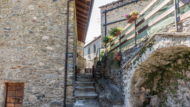 Unes escales de pedra estretes que condueixen a un edifici amb una porta de fusta i una barana metàl·lica.