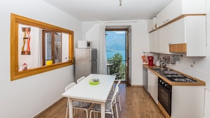 Una cuina compacta amb zona de menjador, nevera, microones, fogó i vistes a les muntanyes per una finestra.