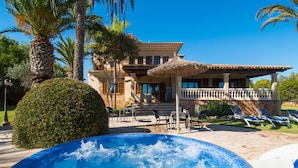 Un espace piscine comprenant un jacuzzi, des chaises longues et un bâtiment doté d’un balcon.