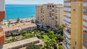 Un hotel frente al mar, con varios pisos, vistas a la playa y un patio con vegetación.