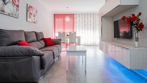 Una sala de estar moderna con un sofá gris, una mesita blanca y un televisor sobre un mueble.