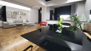 Una sala de estar moderna con una mesa de centro de vidrio, un sofá, un sillón rojo y una planta verde.