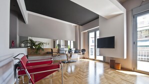 Una habitación de hotel moderna con suelo de madera, un ventanal grande, un televisor de pantalla plana y una silla roja.