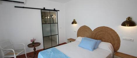 A bedroom with a bed, a chair, a small table with a vase of flowers, and a mirror.