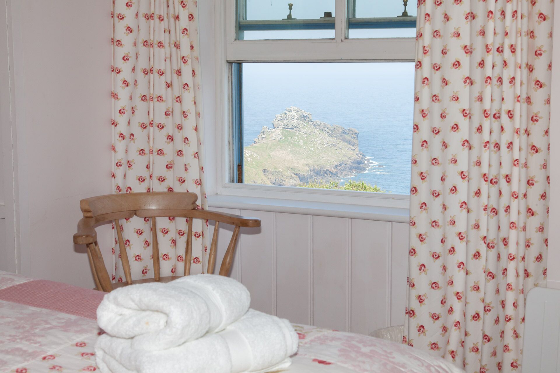 A bedroom with a bed, a chair, and a window with curtains.