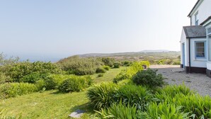 A house with a gravel driveway and a garden with various plants and shrubs. - Holiday cottage with beautiful views over the Cornish sea (St Ives)