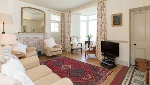 A living room with a fireplace, two armchairs, a sofa, a television, and a large mirror. - Holiday cottage with beautiful views over the Cornish sea (St Ives)