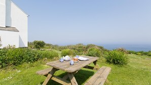 A wooden picnic table with a white building in the background and a view of the sea. - Holiday cottage with beautiful views over the Cornish sea (St Ives)