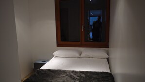 A small, dimly lit bedroom with a single bed, a nightstand, and a window with a wooden frame. - Chatel Centre - 50 M to Ski Lift (Châtel)