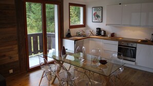 A modern kitchen with glass dining table and chairs, wooden flooring, and a view of the outdoors through large sliding doors. - Chatel Centre - 50 M to Ski Lift (Châtel)