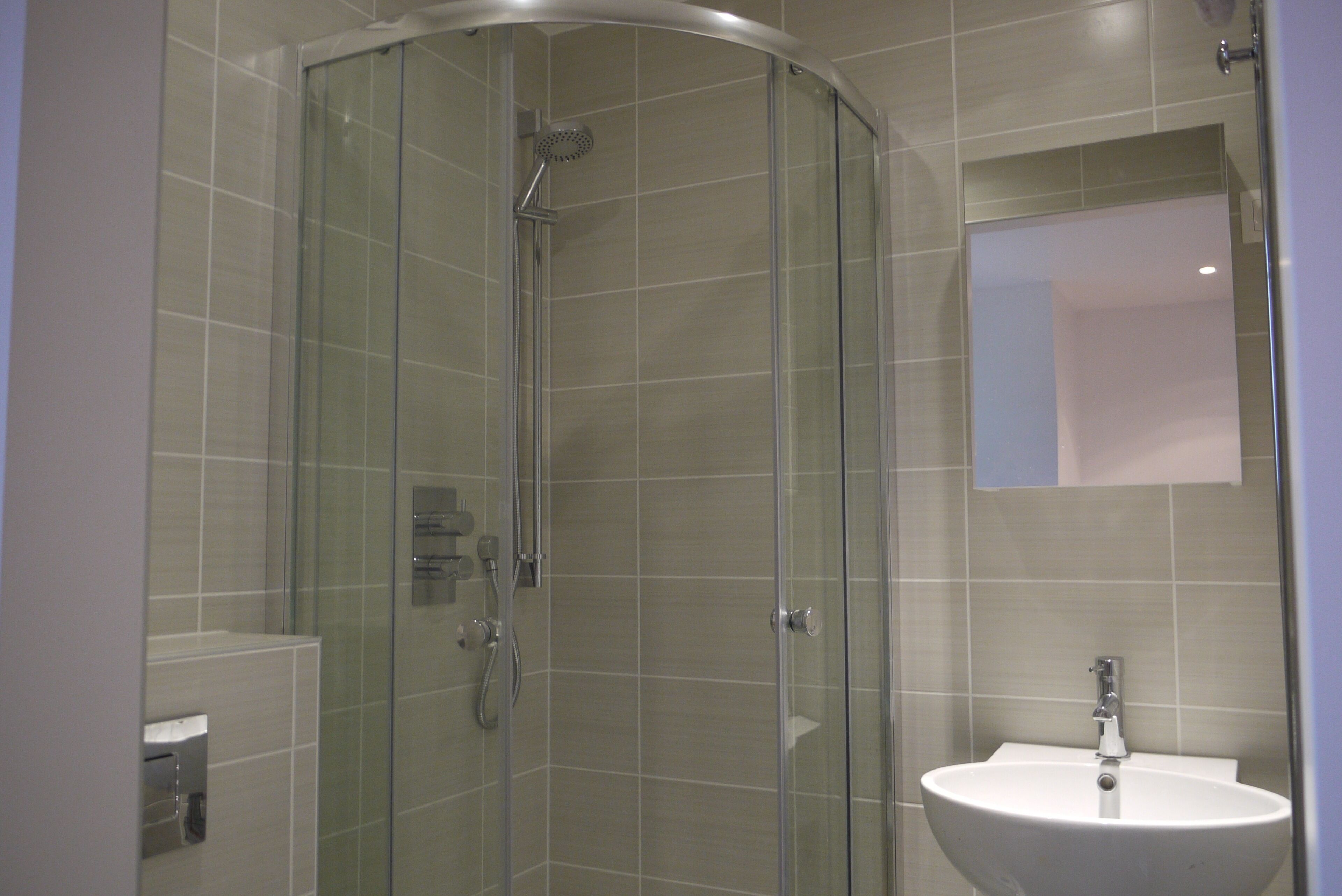 Een moderne badkamer met een douchecabine van glas, een wastafel en een spiegel.