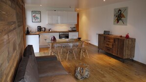 A modern kitchen with white cabinets, a dining area with a glass table and chairs, and a wooden floor. - Chatel Centre - 50 M to Ski Lift (Châtel)