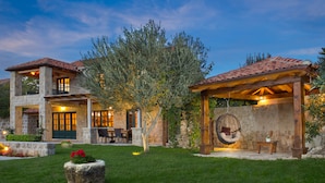 Una casa de piedra de dos plantas con un patio, mobiliario exterior y una silla colgante.
