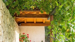 Un espacio de estar al aire libre cubierto con muros de piedra, un banco de madera y una mesa con un jarrón de flores rojas.
