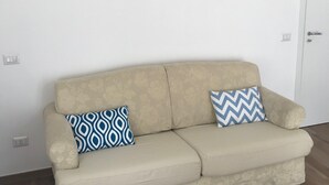 Ein beiges Sofa mit gemusterten Kissen, ein Gemälde darüber und eine weiße Tür zur rechten Seite.