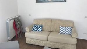 Ein Wohnzimmer mit einem beigen Sofa, zwei gemusterten Kissen, einer Heizung und einem Bild an der Wand.