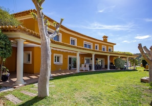 Un edificio amarillo con un porche cubierto, columnas blancas y un césped bien cuidado.