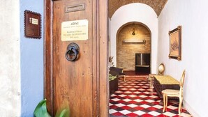 A wooden door with a plaque, a checkered floor, a sofa, and a chair in a room with an arched ceiling. - san gimignano apartment in historical center, courtyard and fast free wifi (San Gimignano)