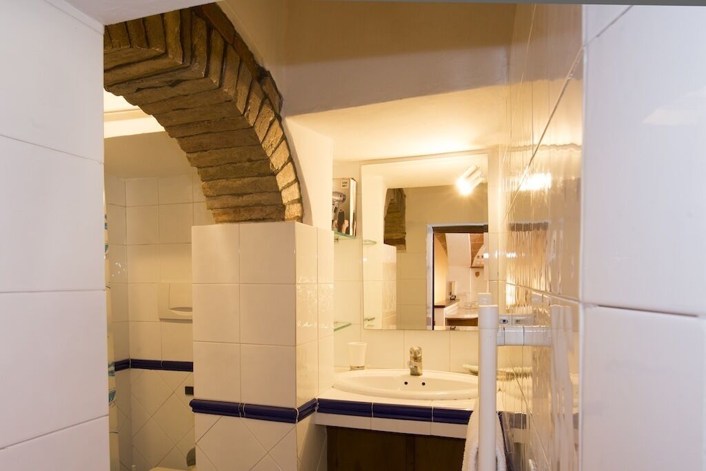 A bathroom with a stone arch, white tiles, a sink, and a mirror.