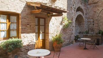 A courtyard with a brick building, a wooden door, a pergola, a table with chairs, and potted plants.