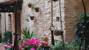 A courtyard with a hanging planter, potted plants, and a brick wall. - san gimignano apartment in historical center, courtyard and fast free wifi (San Gimignano)