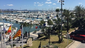 Uma marina com vários barcos atracados, céu claro e algumas pessoas caminhando.
