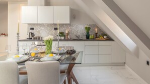 A modern kitchen with a glass dining table, white cabinets, and a tiled backsplash.