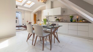 A modern kitchen with white cabinets, a glass dining table, and a skylight.