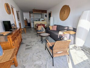 Ein Wohnzimmer mit Sofa, Sesseln, einem Fernseher, einem Essbereich und einer Küche im Hintergrund.