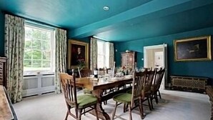 Comedor con una gran mesa dispuesta para seis personas, rodeada de sillas de madera con cojines verdes.