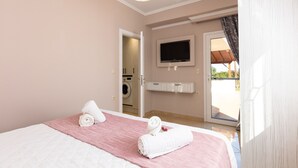 Ein Hotelzimmer mit einem Bett, einem an der Wand befestigten Fernseher, einer Waschmaschine im Hintergrund und einer Schiebetür zu einem Außenbereich.