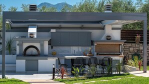 Eine moderne Außenküche mit einer Steinwand, einem Grill und einer Sitzecke mit Stühlen und einem Tisch.
