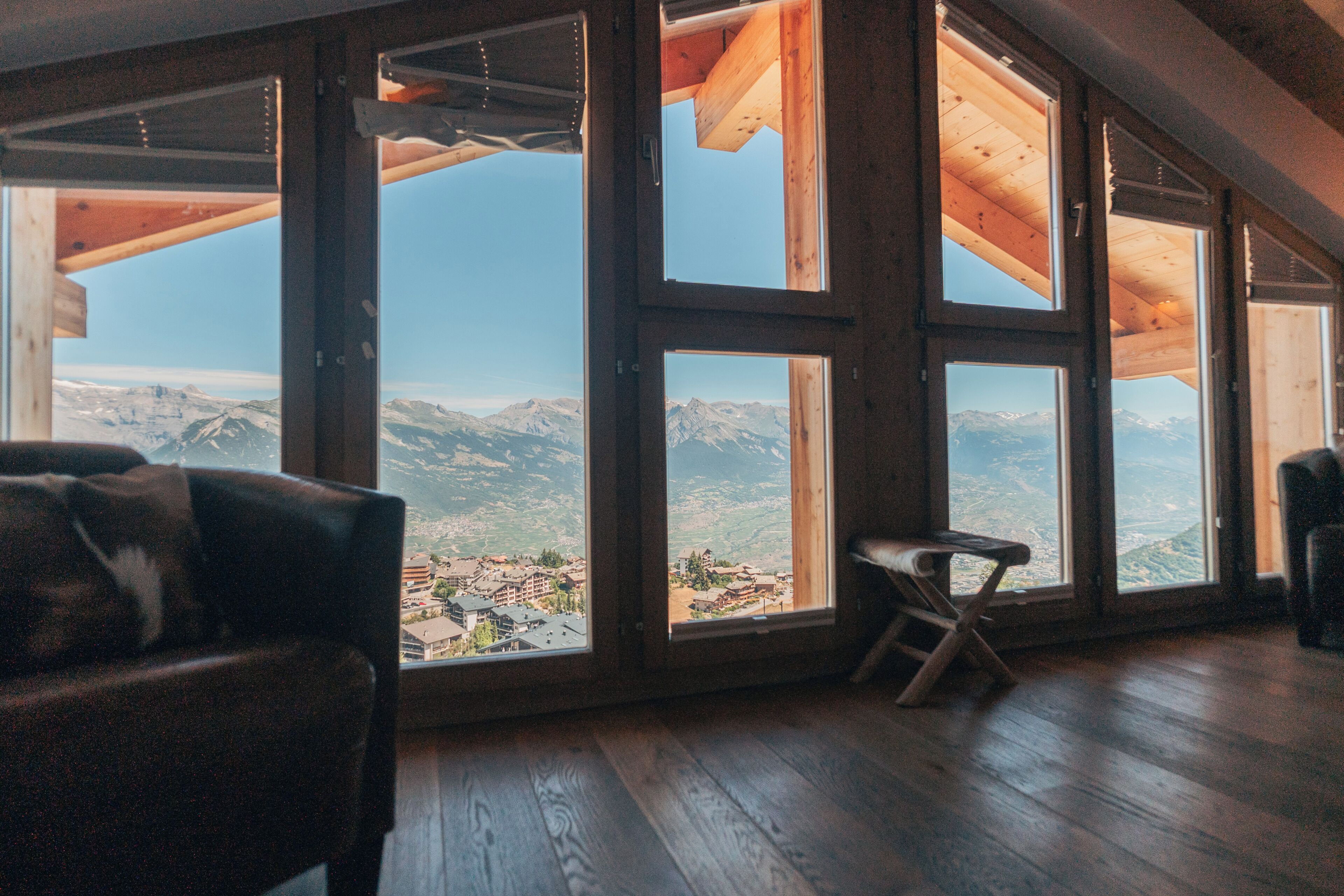 Quarto com grandes janelas que oferecem vista para as montanhas, piso de madeira e uma cadeira.