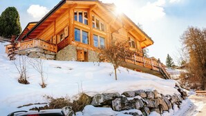 A wooden chalet with a stone foundation, large windows, and a balcony. - Beautiful chalet in the Swiss Alps with stunning views and private hot tub  (Haute Nendaz)
