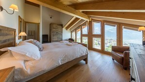 A bedroom with a large bed, wooden beams, a wardrobe, and a view of the mountains. - Beautiful chalet in the Swiss Alps with stunning views and private hot tub  (Haute Nendaz)