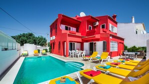 Une villa rouge avec une piscine et des transats jaunes.