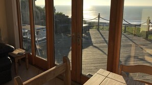 A room with a large glass door leading to a wooden deck overlooking the ocean. - 5 Star Luxury barn conversion overlooking the sea in North Wales (sleeps 2) (Barmouth)