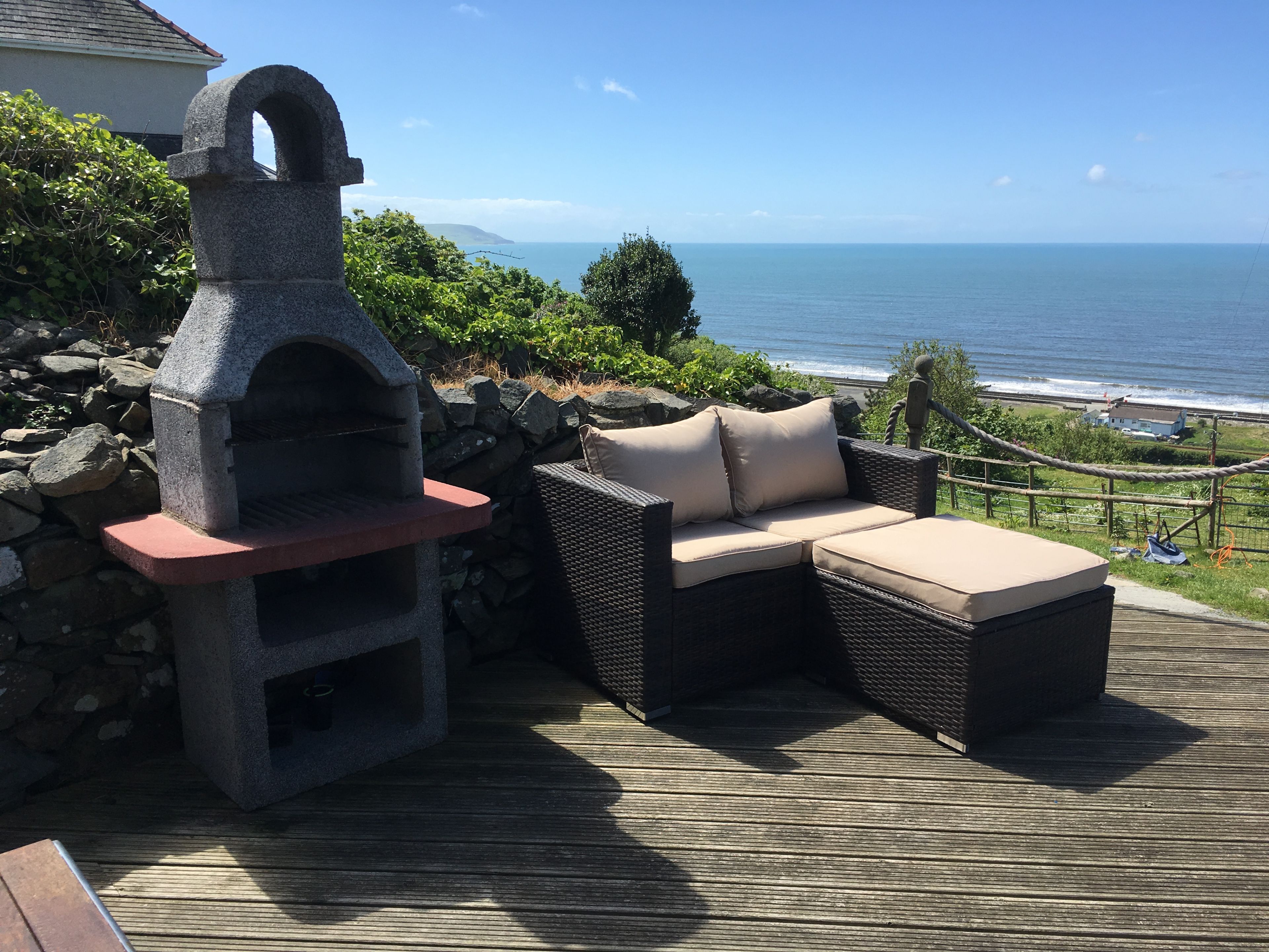 A stone-built outdoor oven, wicker furniture, and a view of the ocean.