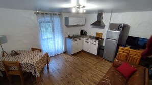 A compact kitchen with a microwave, stove, and sink. There's a dining table with chairs and a sofa with a red pillow. - Nature & tranquility, all year round, a piece of paradise in the Gorges du Tarn (Sainte-Énimie)