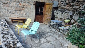 A stone-floored patio with outdoor seating including a table and chairs, a wooden door, and a stone wall. - Nature & tranquility, all year round, a piece of paradise in the Gorges du Tarn (Sainte-Énimie)