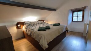 A bedroom with a wooden bed, a nightstand with a lamp, a window with blinds, and a radiator. - Nature & tranquility, all year round, a piece of paradise in the Gorges du Tarn (Sainte-Énimie)
