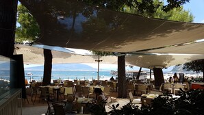 Un área de comedor al aire libre con mesas y sillas, con vista a una playa y al mar.