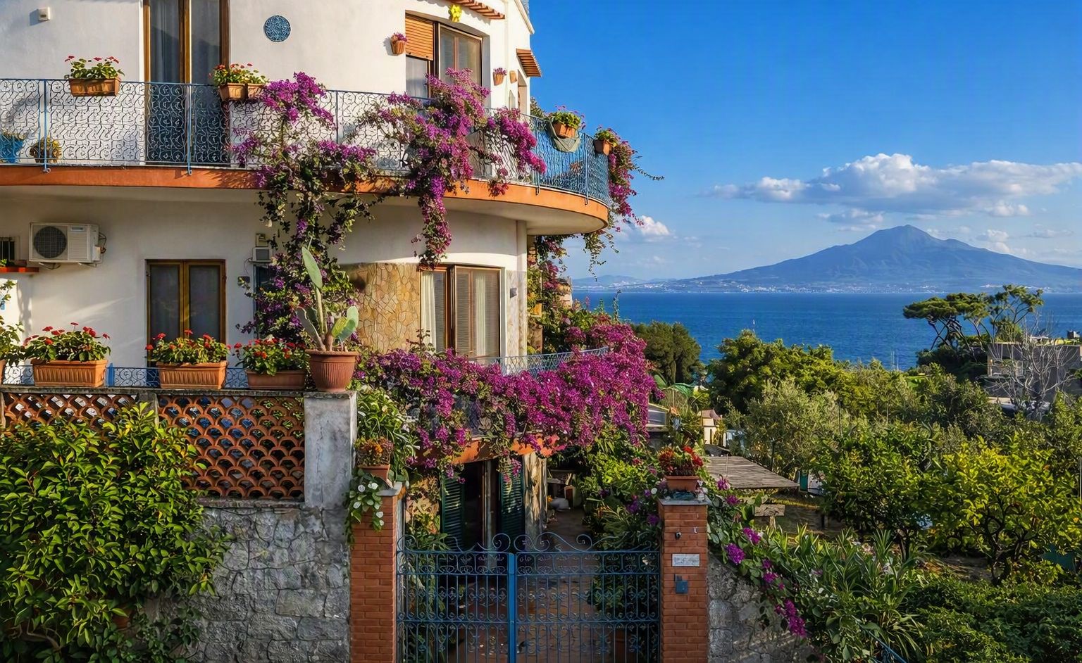 Un immeuble à plusieurs étages doté de balcons, de plantes en pot et offrant une vue sur la mer et une montagne.