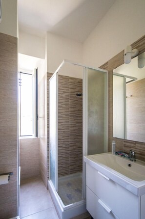 A modern bathroom with a glass shower enclosure, a large mirror, and a white vanity.