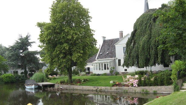 En fridfull vy över en flod med ett hus, en brygga med en båt och frodig grönska.