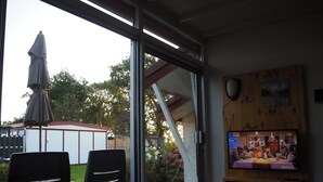 Ett rum med en skjutdörr i glas som leder ut till ett utomhusområde, en tv som är monterad på väggen och ett litet bord med stolar.