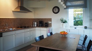 Ett modernt kök med en bänkskiva i granit, vita skåp, ett matbord i trä och ett fönster med utsikt över grönområden.