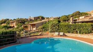 Une piscine dotée d’une terrasse en bois, entourée de murs de pierre et d’une végétation luxuriante.
